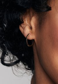 Złota kolczyk w kształcie obręczy z czarnymi akcentami, charakteryzujący się zakrzywionym wzorem. Teksturowana powierzchnia z gładkimi krawędziami i wypolerowanym wykończeniem.