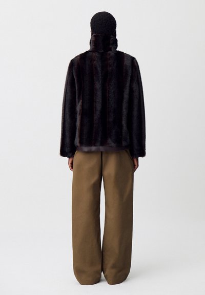 Chaqueta de piel sintética en marrón oscuro con rayas verticales, cuello alto y corte holgado, combinada con pantalones anchos beige.
