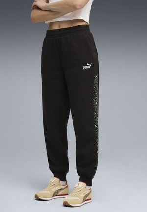 Schwarze Jogginghose mit elastischem Bund und seitlichem Panel im Leopardenmuster. Kombiniert mit beigefarbenen Turnschuhen mit Leopardenakzenten.