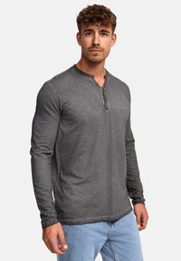 Szary longsleeve henley z okrągłym kołnierzykiem, z dwoma guzikami na plastrze i teksturowanym wyglądzie, zestawiony z jasnoniebieskimi dżinsami.