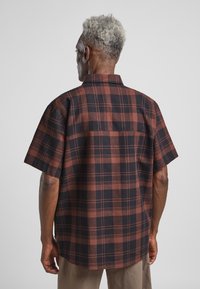 Kurzärmliges kariertes Hemd in Schwarz und Rost mit einem Button-Down-Kragen, featuring eine Passe und dezente Seitenschlitze am Saum.