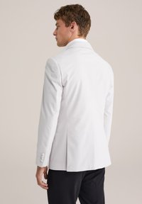 Valge kohandatud bleiser struktuurse disainiga, ühe selja ava ja kolme nupuga varrukatega, kombineeritud tumedate pükstega. Sile tekstuur.