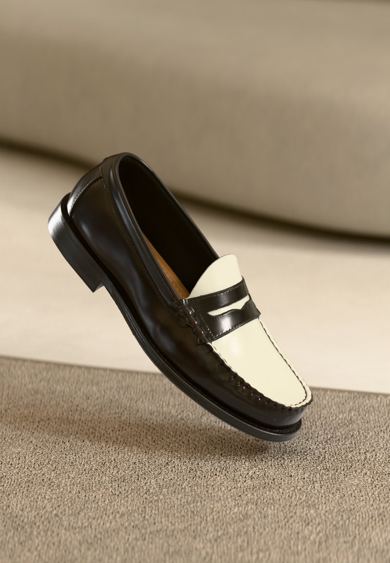 Mocassim de couro preto com uma pala em tom creme e riscas pretas de destaque, apresentando um salto baixo e costura detalhada ao longo das bordas.