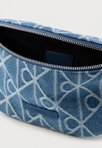 Τσαντάκι από τζιν με μπλε και λευκό αφηρημένο σχέδιο, ασημένιο φερμουάρ και διακριτικό ταμπελάκι με το λογότυπο Calvin Klein στο μπροστινό μέρος.