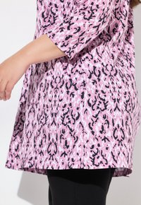 Tunika con stampa animale rosa e nera, dal taglio morbido e con maniche a tre quarti, caratterizzata da un orlo curvo e una texture in cotone morbido.