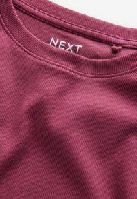 Close-up of a ribbed, dark pink crew neck sweater with a visible white "NEXT" brand label inside the collar.