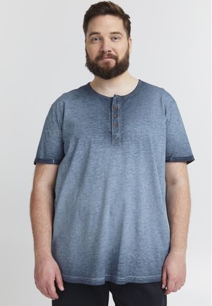 Camiseta azul de manga corta hecha de tela texturada con escote redondeado y cuatro botones marrones a lo largo de la tapeta. Presenta puños enrollados.
