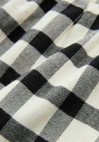 Tessuto a scacchi bianco e nero, caratterizzato da quadrati audaci e una consistenza morbida. La superficie presenta un motivo di colori alternati e linee sottili.