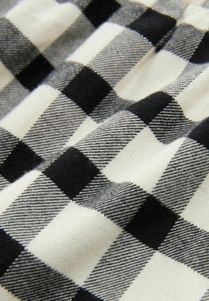 Fekete-fehér kockás textil, merész négyzetekkel és puha textúrával. A felületen váltakozó színek és finom vonalak mintázata látható.