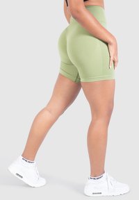 Högmidjade, olivgröna sömlösa shorts med texturerade paneler och en kroppsnära passform, kombinerade med vita sneakers.