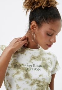 Witte t-shirt met groen tie-dye patroon. Tekst in het groen gedrukt met "je bent een beperkte EDITIE." Korte mouwen en ronde hals.