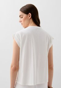 White short-sleeve top made of lightweight fabric, featuring a round neckline and a relaxed fit, smooth texture with minimal design details.