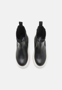 Bottines en cuir noir avec des panneaux élastiques sur les côtés et une languette, dotées d'une semelle en caoutchouc blanche et d'un design épuré et élégant.