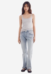 Graues, geripptes Tanktop mit Spitze und Schleife, kombiniert mit hellblauen, geraden Jeans und getragen mit schwarzen, geflochtenen Ballerinas.