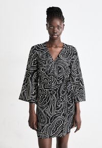 Abito nero con motivo paisley bianco, scollatura a V e maniche a tre quarti a campana. Realizzato in tessuto leggero e texture.