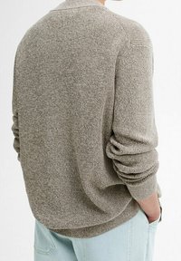 Ljusgrå stickad tröja med en avslappnad passform, ribbade ärmslut och en texturerad yta, i kombination med ljusblå jeans. Baksidan.