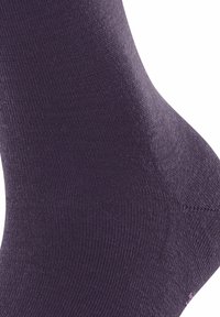 Gros plan sur un pied portant une chaussette unie de couleur violet foncé, montrant le détail du motif en tricot et la zone de la cheville.