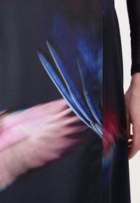 Robe longue en tissu sombre avec des motifs abstraits bleus, roses et violets. Texture lisse avec un design ajusté et un détail de couture sur le côté.