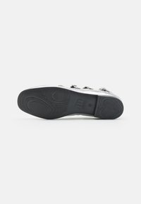 Semelle de chaussure en caoutchouc noir avec un motif de crampons texturé et des bords lisses. Comprend un logo en relief près du talon et un design de support central pour la voûte.