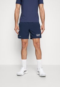 Mornarske športne hlače z elastičnim pasom in belim logotipom. Usklajene z modro majico, belimi nogavicami in belimi športnimi čevlji.