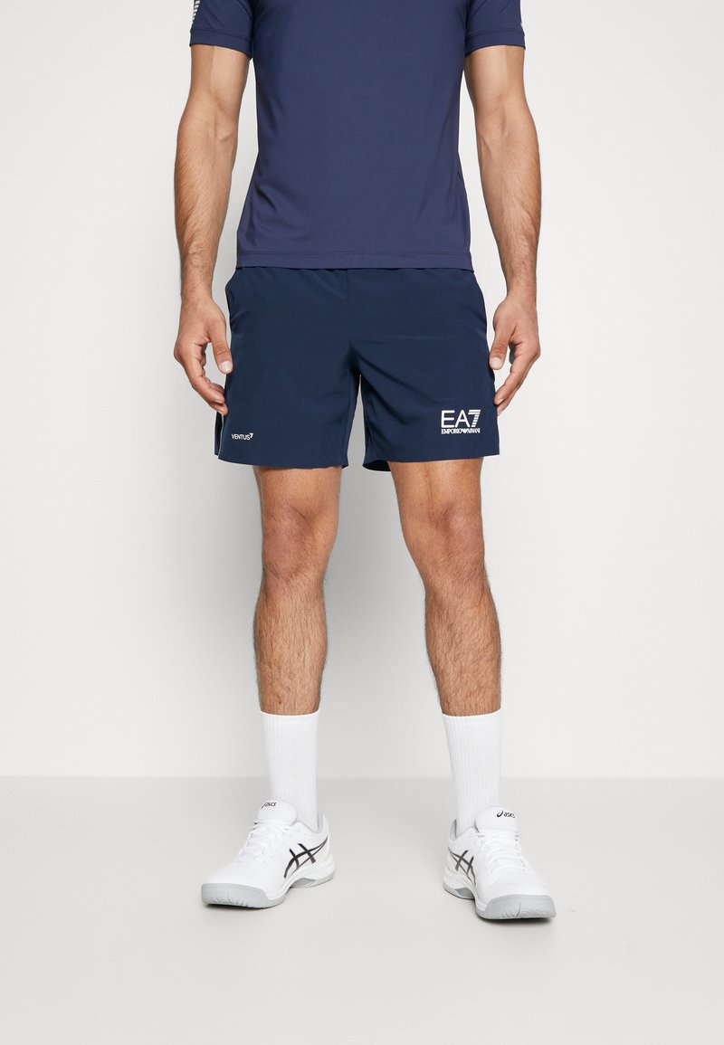 Mornarske športne hlače z elastičnim pasom in belim logotipom. Usklajene z modro majico, belimi nogavicami in belimi športnimi čevlji.