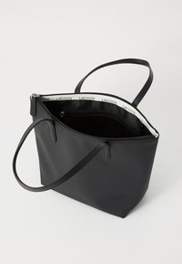 Sac fourre-tout en nylon noir à texture lisse, avec double poignées et fermeture éclair. L'intérieur comprend une doublure de marque et une poche zippée supplémentaire.