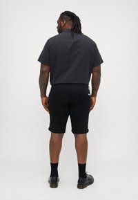 Zwarte kortekorte mouwen shirt met een rechte snit, gecombineerd met zwarte opgerolde shorts. Kenmerken zijn een effen kleur en een casual ontwerp.