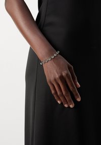 Metal bracelet with alternating shiny and matte spherical beads, worn on a dark-skinned hand against a black dress background.