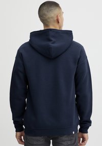 Marineblauwe katoenen hoodie met een grote capuchon, ontspannen pasvorm en geribbelde zoom. Bevat stikseldetails en een klein logotag aan de onderkant.