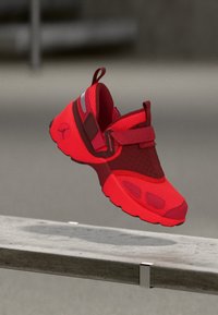 Roter Sportschuh mit Obermaterial aus Mesh und Synthetik, ausgestattet mit einem gepolsterten Kragen, verstellbarem Riemen und strukturierten Akzenten. Leichtgewichtige Sohlenkonstruktion.