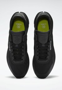 Scarpe da ginnastica nere con design strutturato, caratterizzate da lacci tondi, collo imbottito e soletta verde a contrasto. Marchio Reebok visibile.