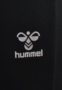 White Hummel merklogo met gestileerde bij boven de tekst op een zwarte stoffen achtergrond.