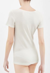 Top corto beige chiaro a maniche corte con scollatura a barca, texture liscia, design leggermente aderente e orlo posteriore più lungo.