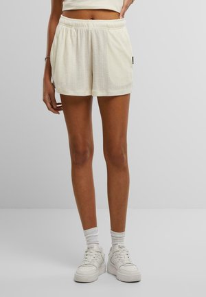 Shorts de couleur crème avec un motif texturé en vertical, une taille élastique et des poches latérales. Portés avec des baskets blanches et des chaussettes.