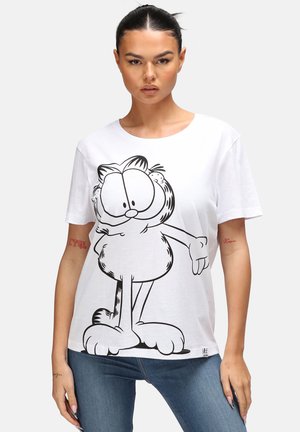 T-shirt en coton blanc avec un grand graphique noir d'un chat de dessin animé aux yeux surdimensionnés et aux pattes énormes. Manches courtes et col rond.
