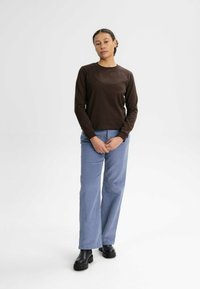 Braunes Langarmhemd kombiniert mit hellblauen weiten Hosen und schwarzen Knöchelboots. Glatter Stoff mit einem schlichten, klassischen Design.