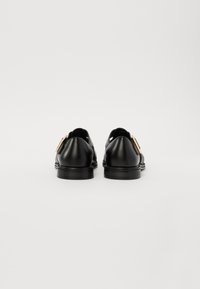 Zwarte leren schoenen met een gladde textuur, ronde neus en een platte zool. Opvallende hardware in goudkleurige tint op de zijkanten.