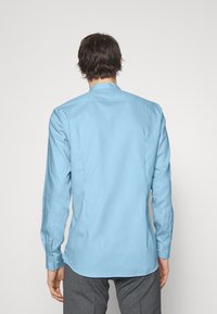 Camicia azzurro chiaro a maniche lunghe con taglio diritto, polsini con bottone e colletto standard. Tessuto liscio e texturizzato; nessun motivo visibile.