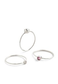 Tre tynde sølv ringe med runde stenindstillinger. En har en klar sten, to har pink sten. Simpelt, minimalistisk design med glat tekstur.