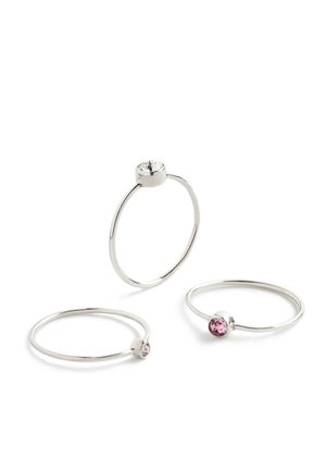 Tre tynde sølv ringe med runde stenindstillinger. En har en klar sten, to har pink sten. Simpelt, minimalistisk design med glat tekstur.