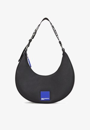 Sac à main noir en forme de croissant avec une large bandoulière noire affichant un texte blanc, et un patch logo carré bleu portant l'inscription "Karl Lagerfeld Jeans".