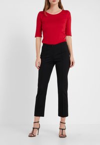 T-shirt rouge ajusté à manches trois quarts associé à un pantalon noir sur mesure, doté d'une fermeture à bouton et d'une texture lisse. Sandales à talons.