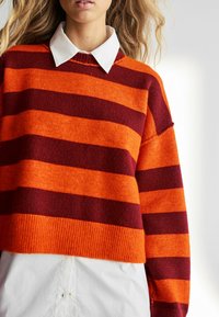 Kootud salliga laiad oranžid ja burgundia toonid, soonikkoes äär, ja valge kraega särk all. Pehme tekstuur.