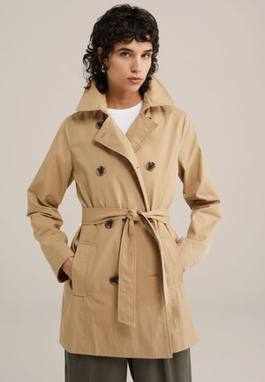 Trench coat beige chiaro con cintura in vita, bottoni doppi, e tasche laterali, realizzato in un tessuto liscio e strutturato.
