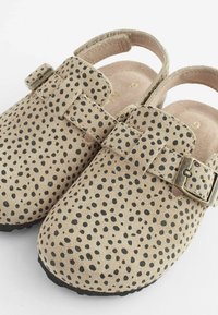 Beige Wildlederclogs mit schwarzen Punkten, verstellbarem Riemen mit Metallverschluss, offenem Fersenbereich und strukturiertem Gummisohle.