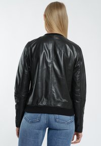 Sorte læderjakke med en glat tekstur, ribbet kant og lange ærmer. Har minimal syning og en tætsiddende design.