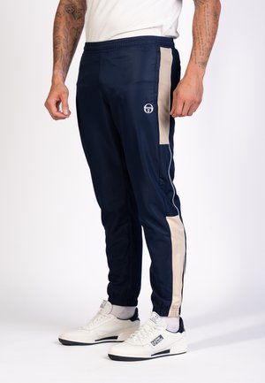 Marineblauwe sportbroek van lichtgewicht materiaal met beige zijpanelen, elastische taille en getailleerde boorden. Logo op de voorkant.