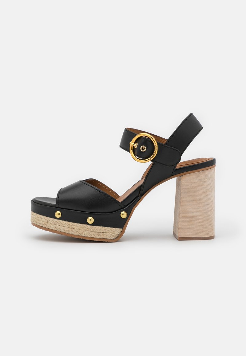 Sandale plateforme en cuir noir avec boucle dorée et clous, détail tressé sur la plateforme, et talon en bois clair sur fond blanc.