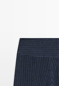 Jupe bleu foncé à fines rayures avec taille haute et détail de panneau avant superposé sur fond blanc.