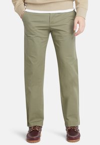Chinos verde oliva con un diseño de pierna recta, superficie suave y bolsillos laterales, combinados con zapatos náuticos marrones con cordones y suelas de goma.
